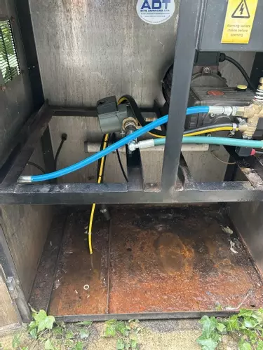 Internal view of a cold pressure washer cabinet showing contamination and moisture buildup caused by an unsealed plastic water tank. Constant condensation from hot water feed led to corrosion, dirt accumulation, and poor system hygiene.